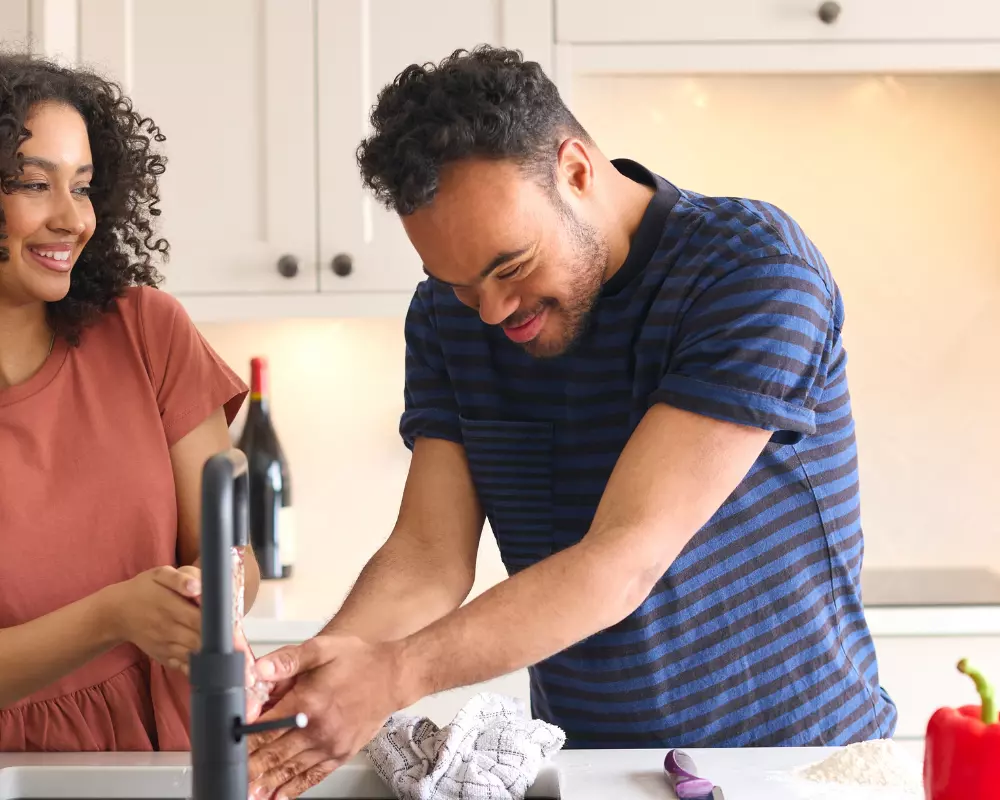 Happy disabled man with down syndrome washing hands in kitchen with support worker
