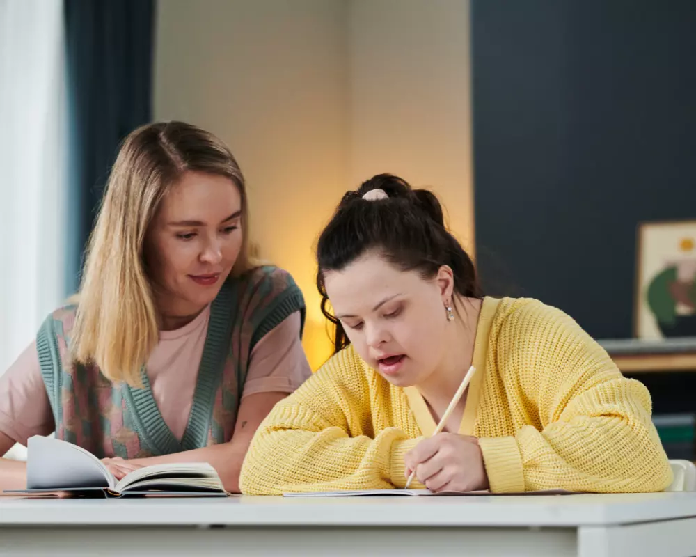 Woman with down syndrome writing next to support worker